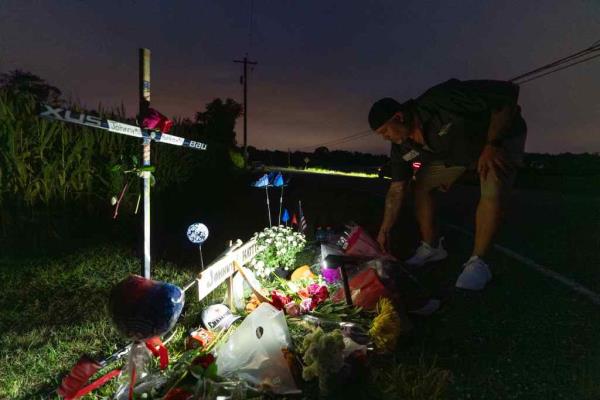 Man kneeling next to a makeshift memorial of cross and flowers at the corner of Pennsville Auburn Road and Stumpy Lane
